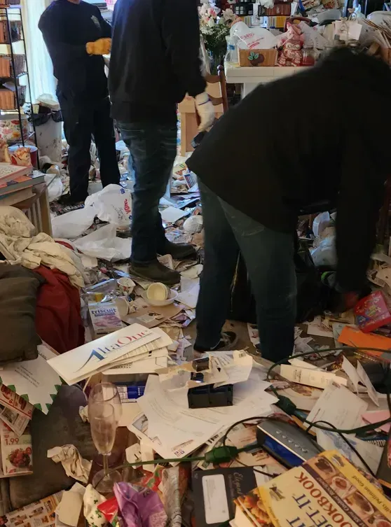 Two crew members clearing a Bakersfield living room packed to the floor with paper, packaging and household clutter.